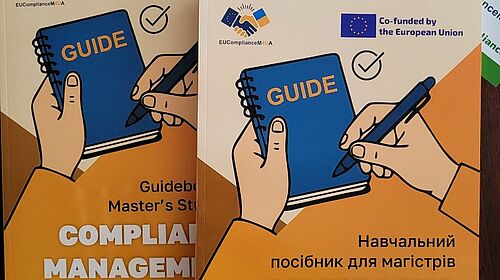 Englisches und ukrainisches Compliance-Guidebook liegen mit Flyern und Projektmaterialien auf einem Tisch.