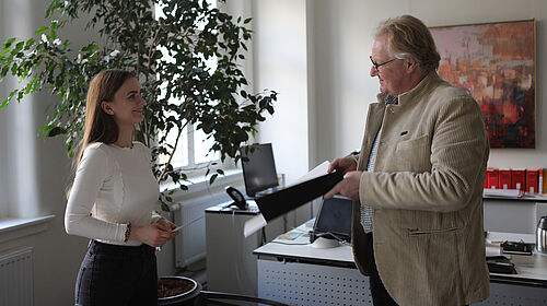 Die Ausgezeichnete ist im Büro des Rektors der Hochschule Wismar zu sehen, wie sie aus seinen Händen die Urkunde erhält.