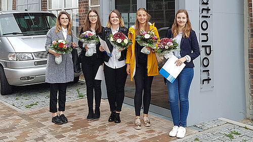 Auf dem Bild sind die fünf ausgezeichneten Studentinnen mit Blumensträußen zu sehen.