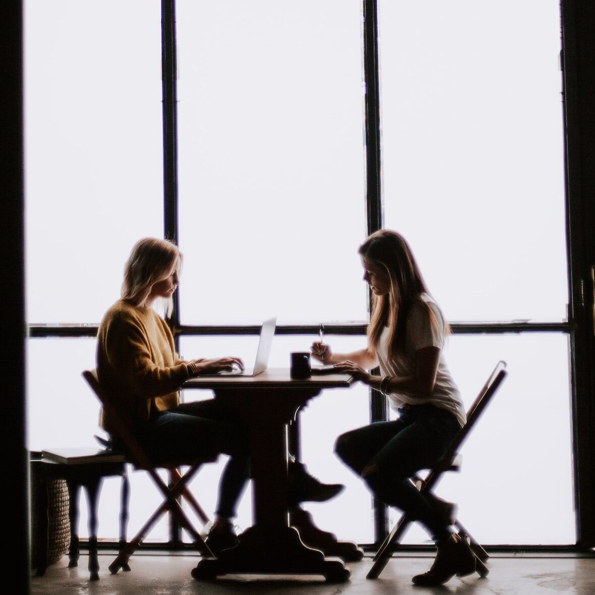 Zwei Frauen sitzen sich an einem Tisch gegenüber, Gegenlichtfotografie, starker Kontrast