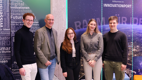 Fünf Personen stehen nebeneinander und blicken lächelnd in die Kamera. Im Hintergrund ist eine Wand mit dem Schriftzug „Innovation Port“ und grafischen Elementen zum Thema Innovation und Raumfahrt zu sehen.