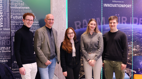 Five people are standing side by side and smiling at the camera. In the background, there is a wall with the writing ‘Innovation Port’ and graphic elements on the topic of innovation and space travel.