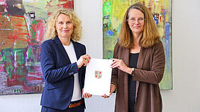 Es ist die Professorin zu sehen, die gemeinsam mit der Ministerin, die neben ihr steht, ihre Ernennungsurkunde in der Hand hält.