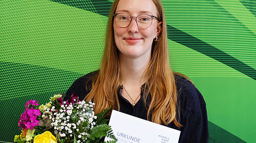 Lara Baumbach hält Urkunde und Blumenstrauß nach der Auszeichnung ihrer Bachelorarbeit.