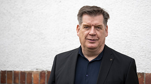 Professor Lau steht vor einer Hauswand im Freien. 