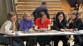 Fünf Frauen sitzen an einem Tisch und schauen auf Dokumente vor ihnen. Die Stimmung ist gelöst. 