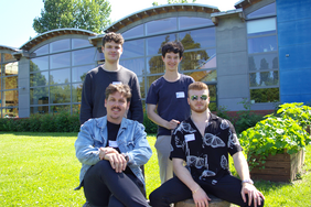 Vier junge Männer, Bastian Gabriel, Marcel Boelsch, Karl Schlüter und Elliott Steinberg, posieren gemeinsam im Grünen vor der StartUpYard der Hochschule Wismar. Sie entwickelten ein GPS-Backup-System, das ohne Satelliten funktioniert.