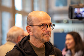 A: Der Professor ist leicht seitlich im Porträt zu sehen, wie er konzentriert in Richtung Kamera schaut.