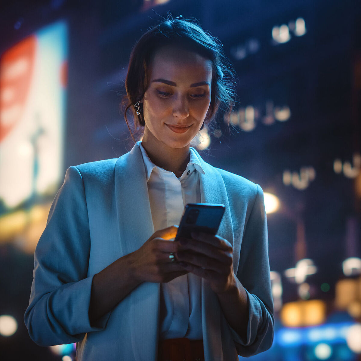 Frau auf der Straße, Lichter der Großstadt, sie blickt auf ihr Handy