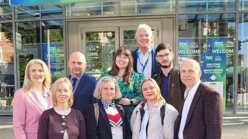 DigiTechPort2030 project partners at TOC Europe 2026 in Hamburg Several project partners from the DigiTechPort2030 consortium are standing outside the entrance to TOC Europe 2026 in Hamburg. Above them hangs a large welcome sign for the trade fair.