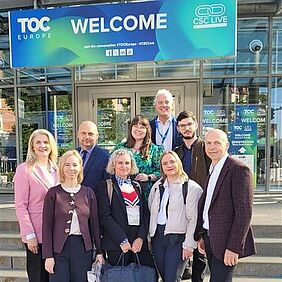 Projektpartner von DigiTechPort2030 bei der TOC Europe 2026 in Hamburg Mehrere Projektpartner des DigiTechPort2030-Konsortiums stehen vor dem Eingang der TOC Europe 2026 in Hamburg. Über ihnen befindet sich ein großes Willkommensschild der Fachmesse.