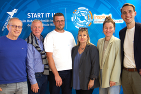 Sechs Jurymitglieder stehen nebeneinander vor einem blauen Hintergrund mit dem Logo des Robert-Schmidt-Instituts und des INSPIRED-Wettbewerbs. Alle blicken in die Kamera und lächeln.