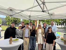 Studierende präsentieren Projektergebnisse Eine Gruppe Studierender steht zusammen mit Prof. Dr. Jantina Nord unter einem Pavillon vor der Hochschulwiese.