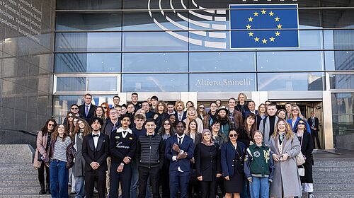 Gruppe internationaler Teilnehmender steht vor dem Gebäude des Europäischen Parlaments in Brüssel und blickt in die Kamera.