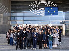 Group of international participants standing in front of the European Parliament building in Brussels, facing the camera.