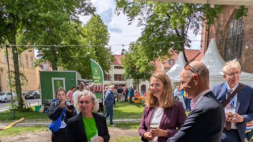 Personengruppe auf dem Veranstaltungsgelände vor der Kirche. Laima Gerlitz im Gespräch mit der Ministerin Bettina Martin und Prof. Junghanß von der Universitätsmedizin Rostock.
