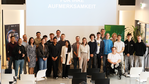 Group photo of about 25 people including students, jury members, and university staff. They are standing together in the InnovationPort Wismar presentation space in front of a screen with the words "Für Ihre Aufmerksamkeit" (“Thank you for your attention”).