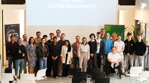 Gruppenfoto mit rund 25 Personen, darunter Schülerinnen und Schüler, Jury und Hochschulvertretende. Sie stehen gemeinsam im Veranstaltungsraum des InnovationPort Wismar vor einer Leinwand mit der Aufschrift „[...] für Ihre Aufmerksamkeit“.