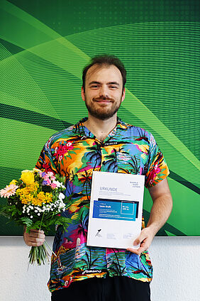 Leon Kreft präsentiert Urkunde und Blumenstrauß nach der Ehrung seiner Bachelorarbeit.